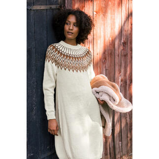 Frau in einem langen, hellen Kleid mit gestricktem Muster, hält einen Pullover in der Hand.