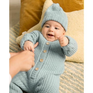 Baby in hellblauem Strampler und Mütze, spielt auf einem Teppich.