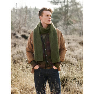 Mann in grünem Schal steht im Wald, lächelt in die Kamera.