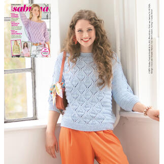 Frau posiert in einem blauen, gestrickten Pullover mit orangefarbenen Hosen.
