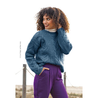 Blauer Pullover aus Ingenua, Modell mit Locken und lächelnd in der Natur.