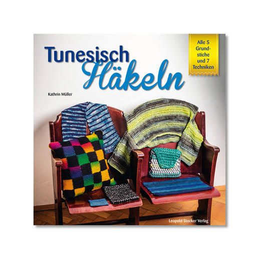 Buch 'Tunesisch Häkeln' mit diversen gehäkelten Kissen und Decken auf einem Stuhl.