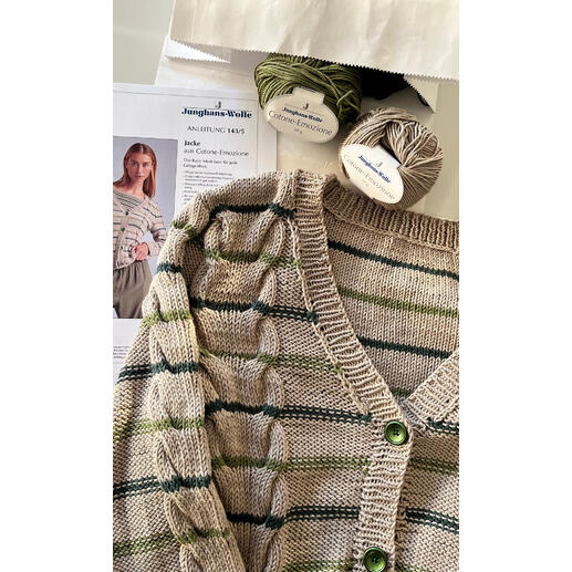 Wolljacke mit grünen Streifen und Knöpfen auf einem Tisch mit Garn und einer Anleitung.