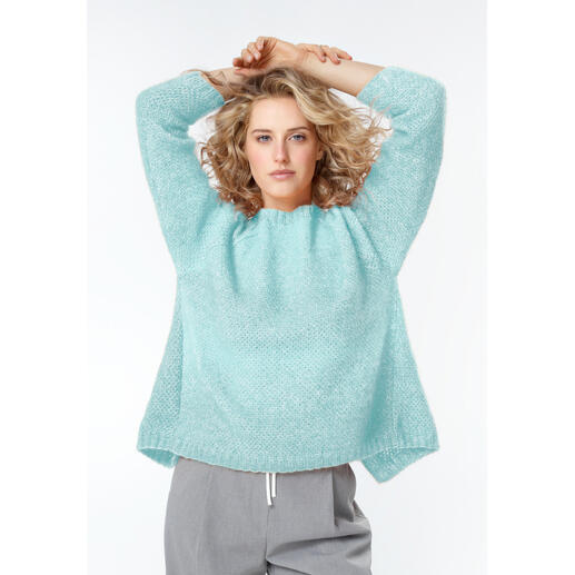 Frau in hellblauem Pullover aus Alpafluffy mit lockerer Passform, lächelt in die Kamera.