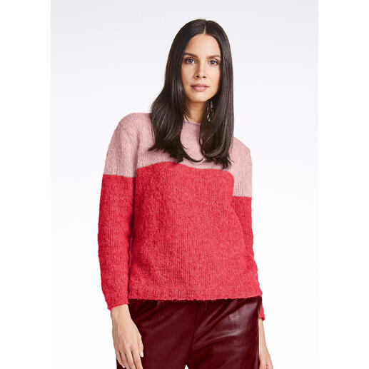 Frau in einem Farbblock-Pullover in Rosa- und Rottönen, lächelnd in die Kamera.