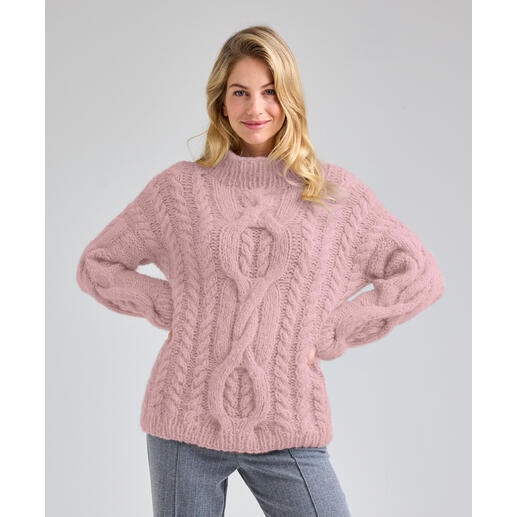 Frau in einem strukturierten, rosa Pullover mit Zopfdesign, posiert freundlich.