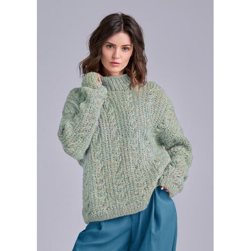 Frau in einem grünen, strukturierten Pullover, schaut wahrhaftig in die Kamera.