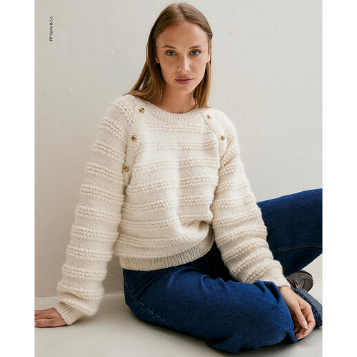 Frau sitzt in einem weißen Pullover aus Phil Baby Alpaga von Phildar.