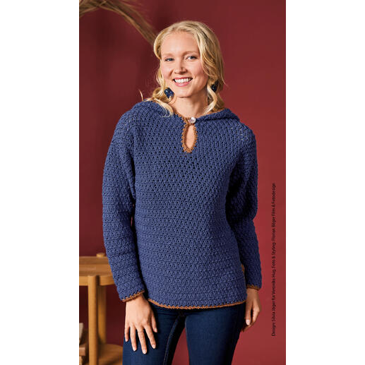 Fröhliche Frau in einem blauen gehäkelten Kapuzenpullover aus Merino Stretch von Woolly Hugs.