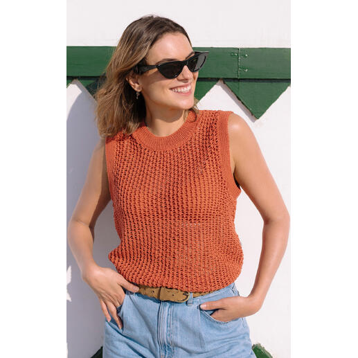 Frau in rotem Häkeltop mit den Händen in die Hüften gestützt, vor einer weißen Wand.