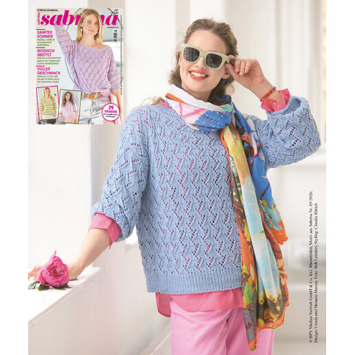 Frau in einer blauen, luftigen Strickjacke hält eine Blume und posiert.