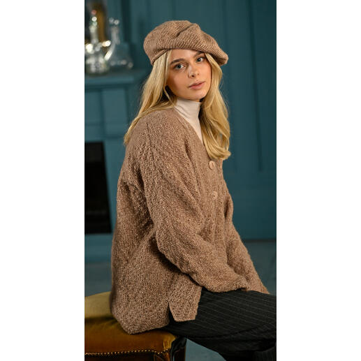 Beiger Cardigan mit Baske, Modell sitzt auf einem Stuhl mit einer Mütze.
