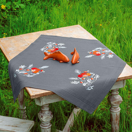 Tischdecke mit Mohnblumenmotiven auf einem Holztisch im Freien.