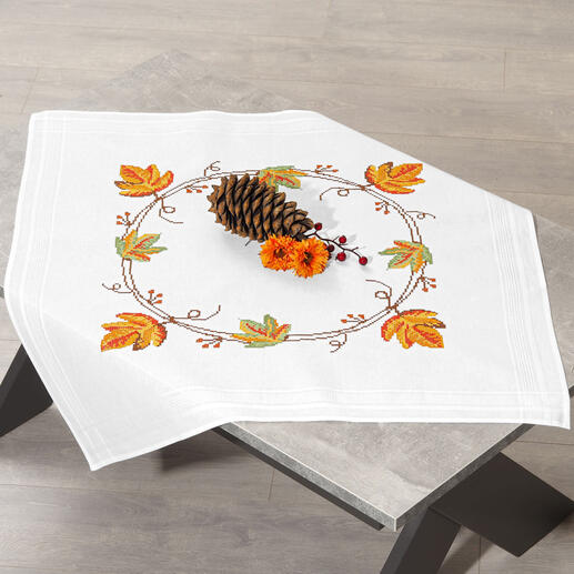 Tischdecke mit herbstlichen Blättern und einer festen Deko auf einem Tisch.