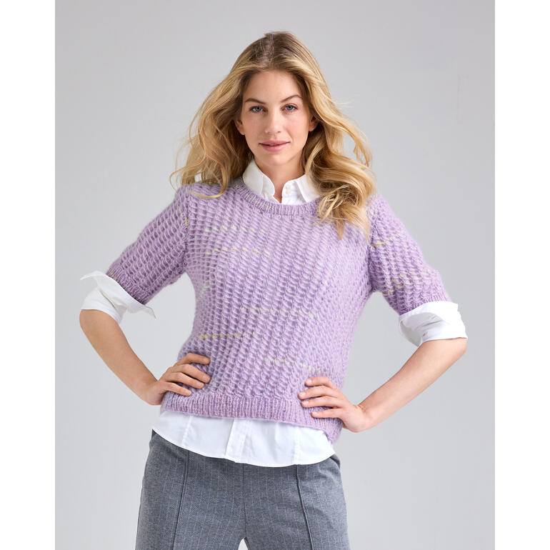 Frau in einem lila Pullover mit kurzen Ärmeln, steht selbstbewusst mit verschränkten Händen.