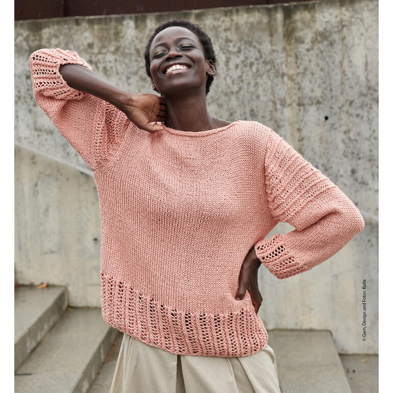 Frau in rosafarbenem Pullover mit lässigem Look, lächelt in urbaner Umgebung