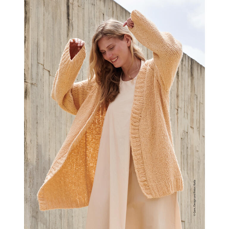 Frau in beigefarbener Jacke, die geöffnet getragen wird, lächelt vor trockener Wand