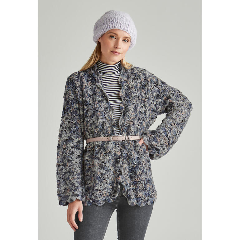 Frau in einer gehäkelten Jacke mit einem Gürtel, steht vor einem hellen Hintergrund.