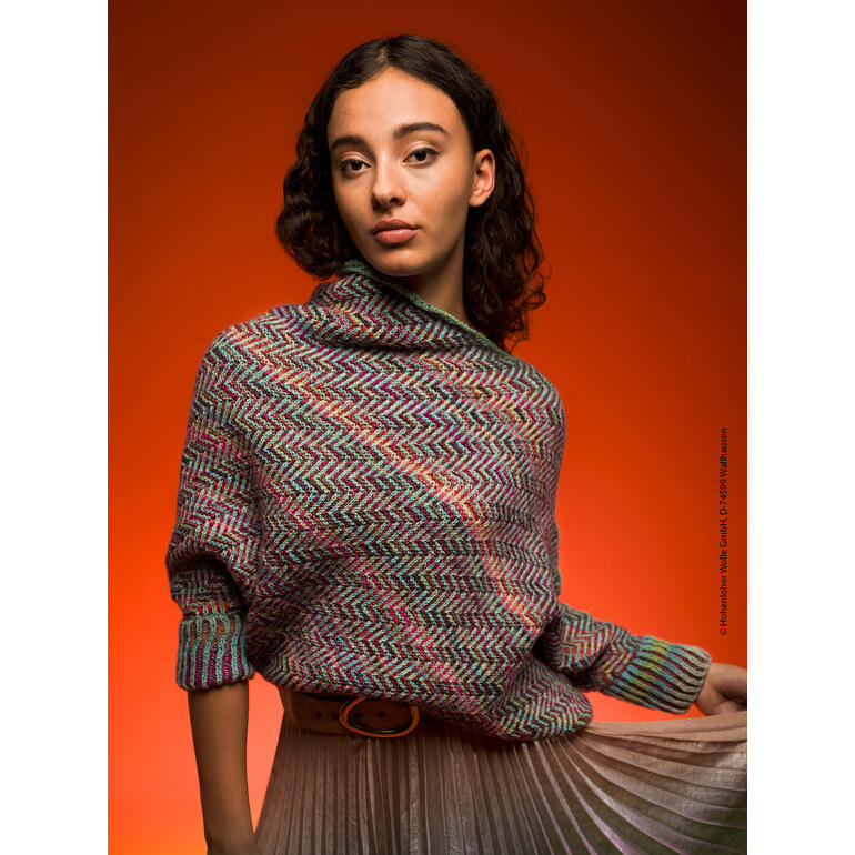 Frau trägt einen bunten Pullover mit Wellenmuster, steht vor einem orangefarbenen Hintergrund und schaut in die Kamera.