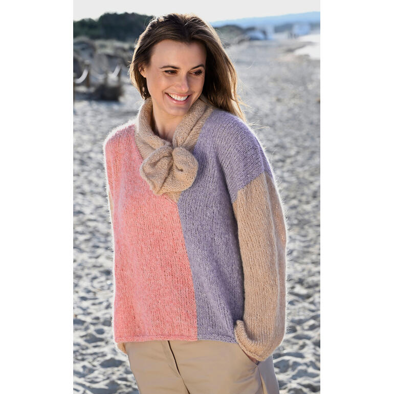 Frau in buntem Pullover aus Linie 550 Prato, mit einer Schleife, sitzt am Strand.