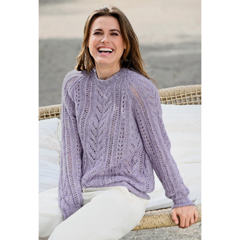 Frau in lila Pullover mit Lochmuster, lächelt fröhlich in einer natürlichen Umgebung.