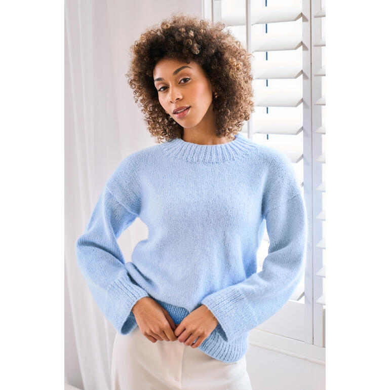 Frau in hellblauem Pullover aus Softest Alpaca, lächelt sanft.