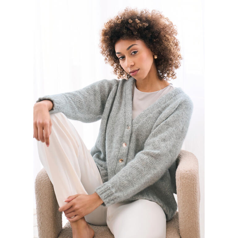 Frau in grauer Jacke aus Softest Alpaca, sitzt auf einem Sessel.