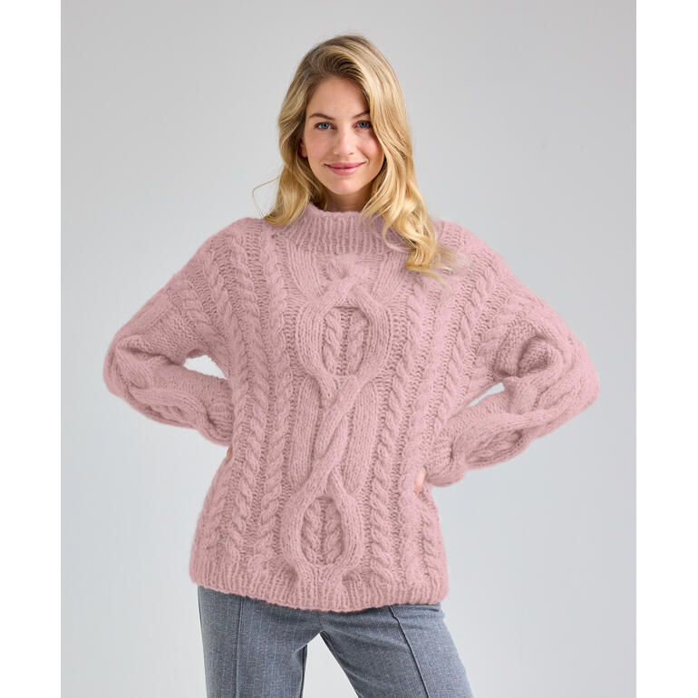 Frau in einem strukturierten, rosa Pullover mit Zopfdesign, posiert freundlich.