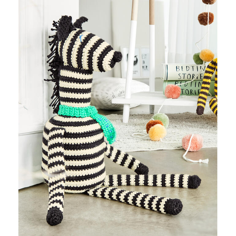 Häkelzebra ‚Zack‘ aus Cotonara, sitzend mit türkisfarbener Schärpe.