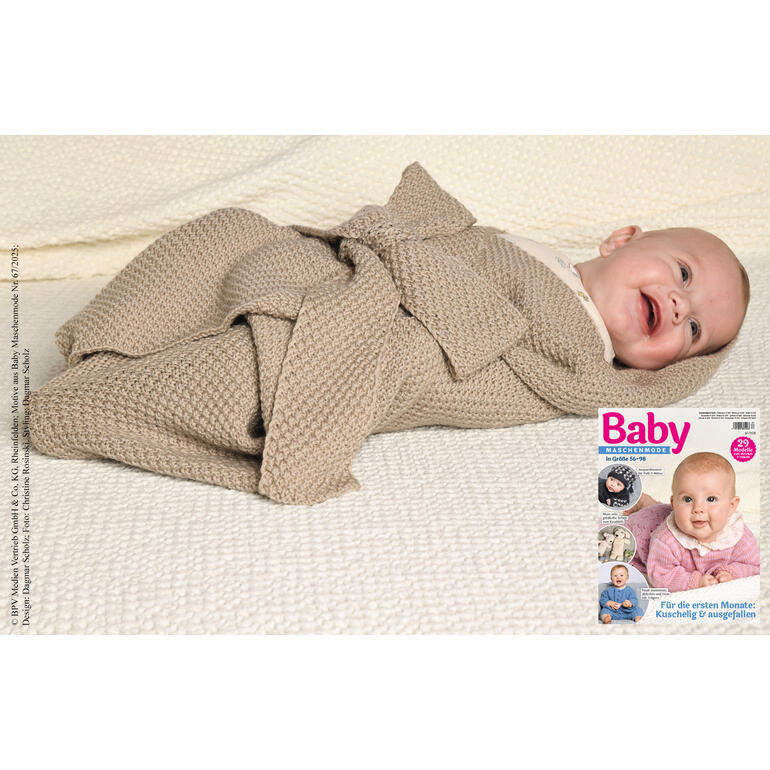 Lächelndes Baby in einem Pucktuch aus Nuovo Merino auf einem weißen Strickstück