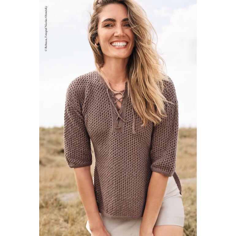 Frau in braunem Tunika aus Elida lächelt glücklich auf einer Wiese.