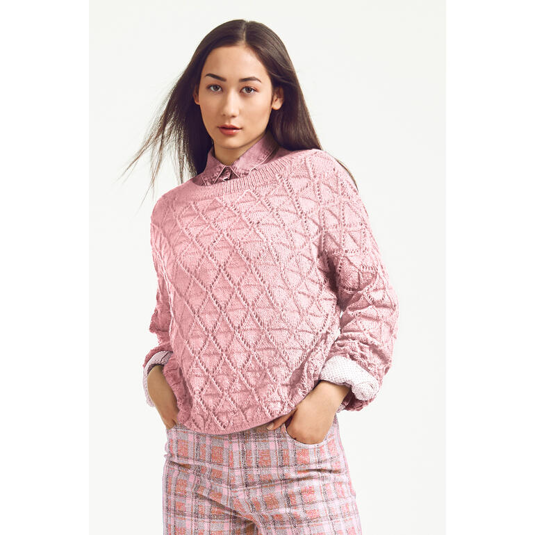 Frau mit rosa Pullover aus Seidana, trägt ein Hemd darunter, vor neutralem Hintergrund.