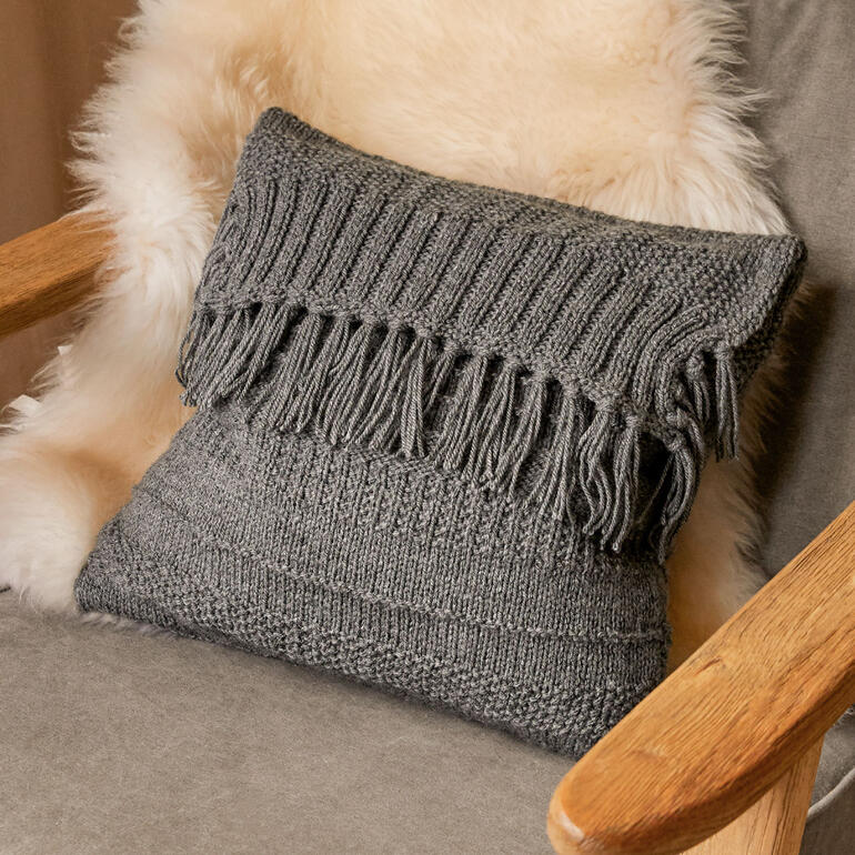 Gestricktes Meditationskissen mit Fransen auf einem Stuhl.