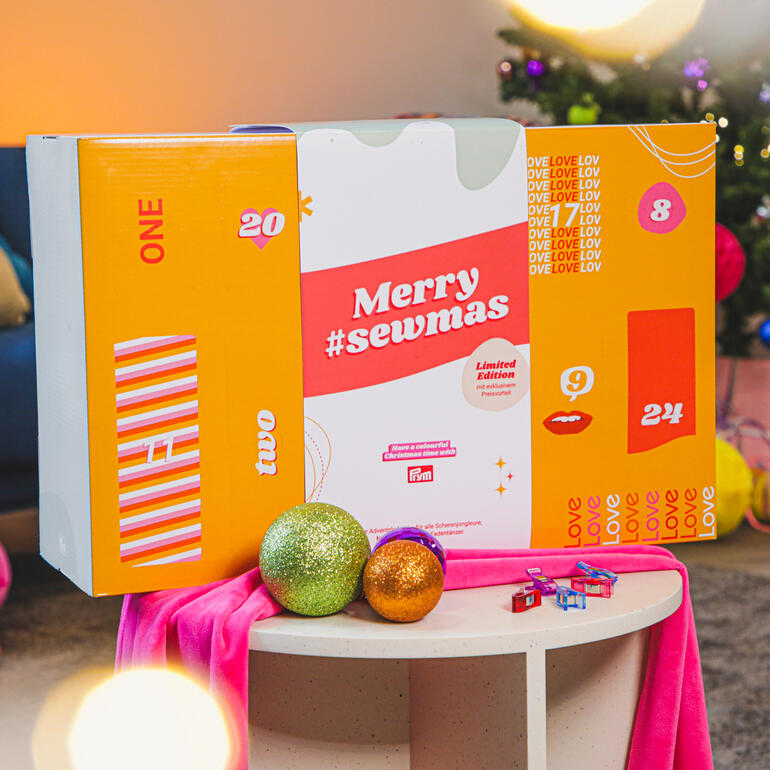 Prym Adventskalender 22 in buntem Design auf einem Tisch vor einem Weihnachtsbaum.