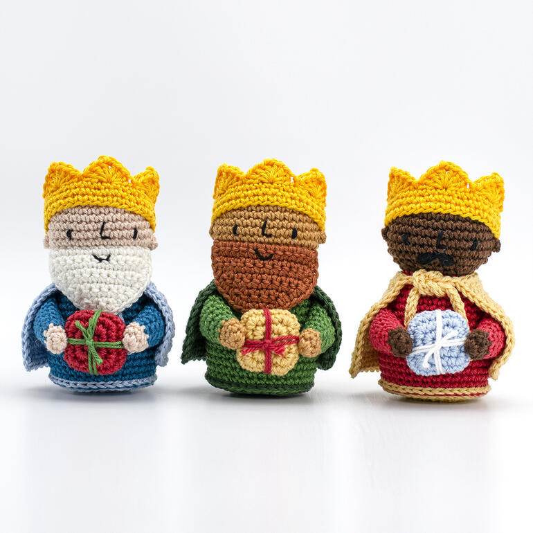Drei gehäkelte Könige mit goldenen Kronen, jeder mit einem Geschenk in der Hand.