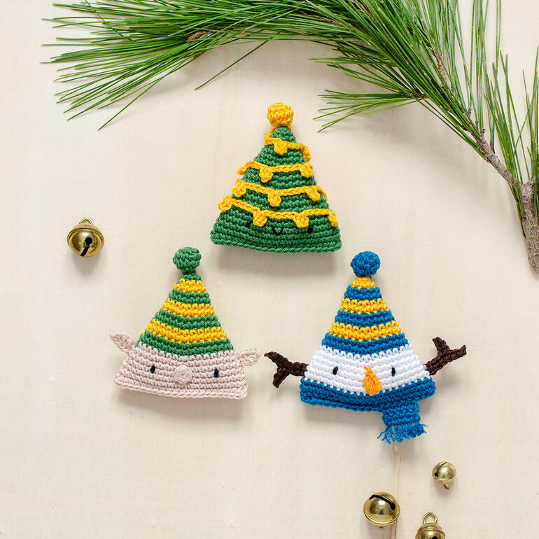 Drei gehäkelte Weihnachtsmützen: ein Weihnachtsbaum, ein Schneemann und ein Elf.