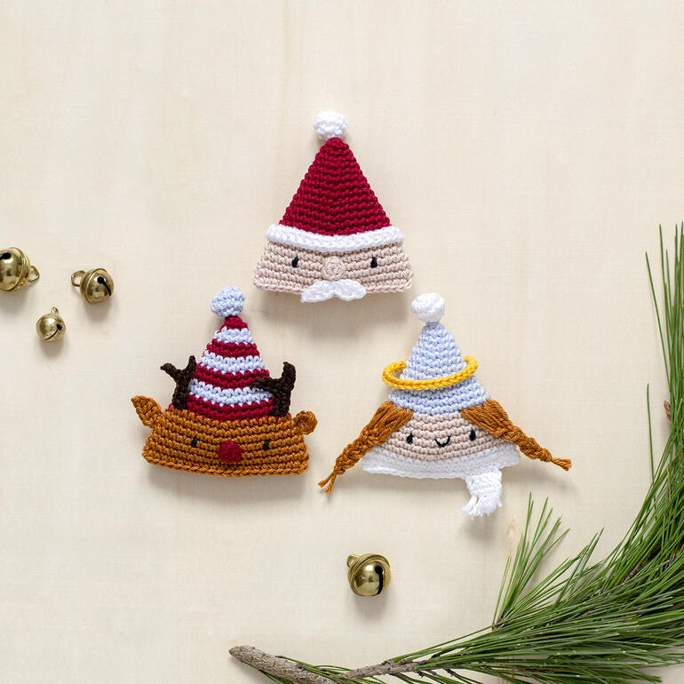 Drei gehäkelte Weihnachtsmützen: ein Schneemann, ein Engel und ein Rentier.