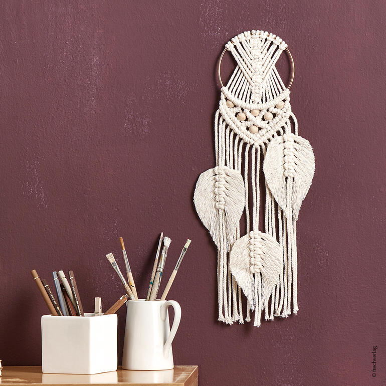 Makramee-Set mit Traumfänger, dekoriert mit geflochtenen Blättern auf rotbraunem Hintergrund.