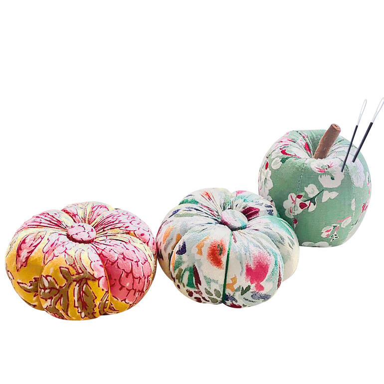 Drei farbige Nadelkissen in Kürbisform auf einem Tisch.