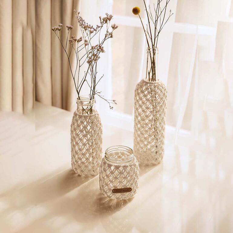 Makramee-Set zur Glasdekoration mit Blumen in Flaschen auf einem Tisch.