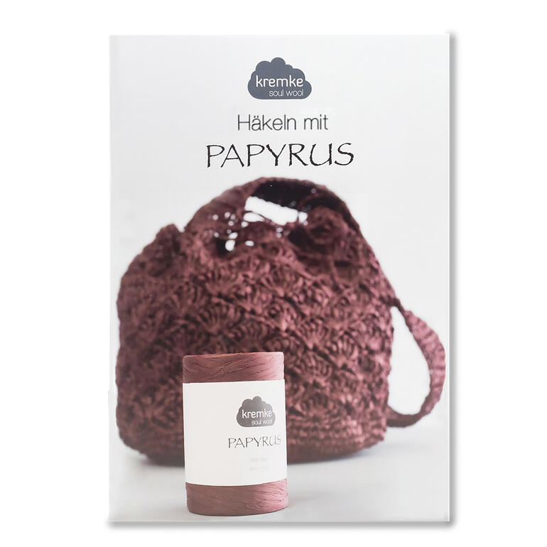 Heft über Häkeln mit Papyrus und einer Tasche im Hintergrund.