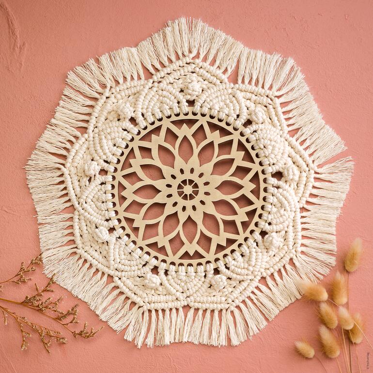 Wandbehang aus Makramee mit floralen Mustern auf einem rosa Hintergrund.