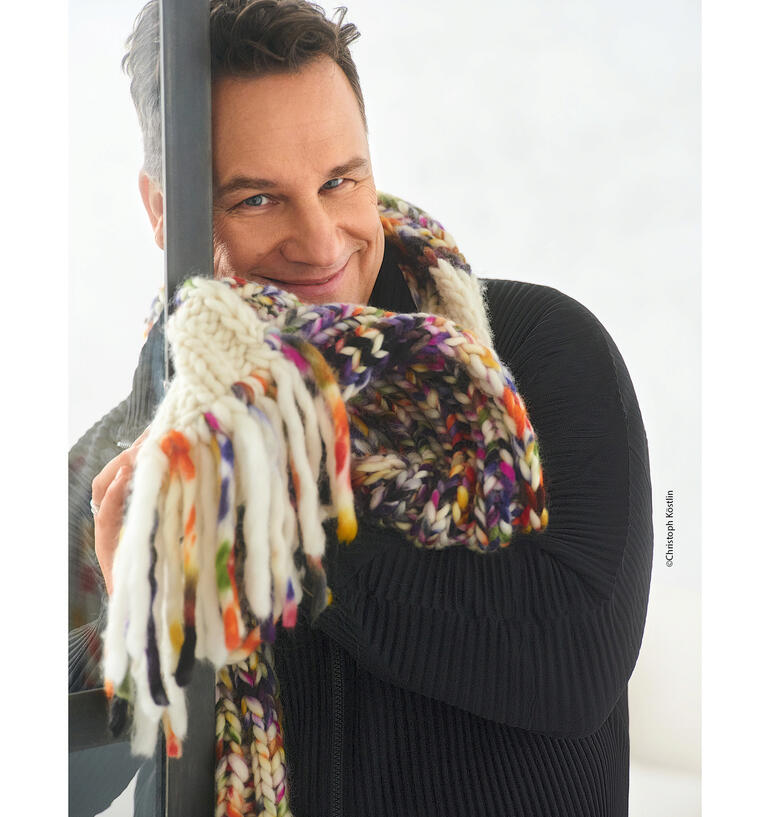 Lächelnder Mann mit buntem Schal vor einem Fenster