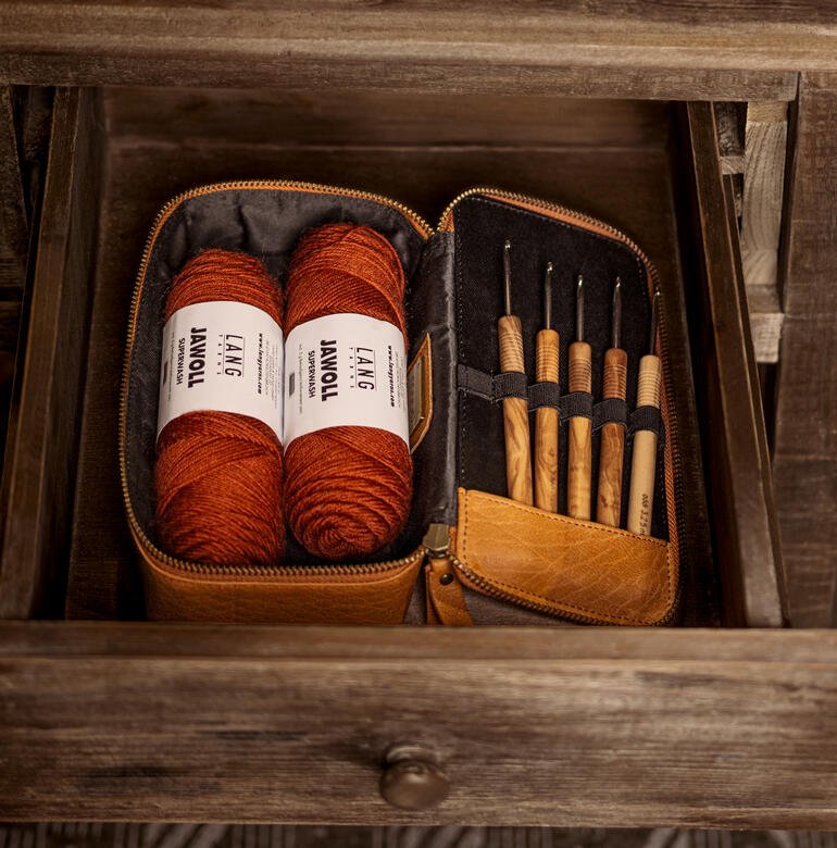 Muud Mappe Hope in Whisky-Farbe mit Garn und Werkzeugen im offenen Etui auf einem Tisch.