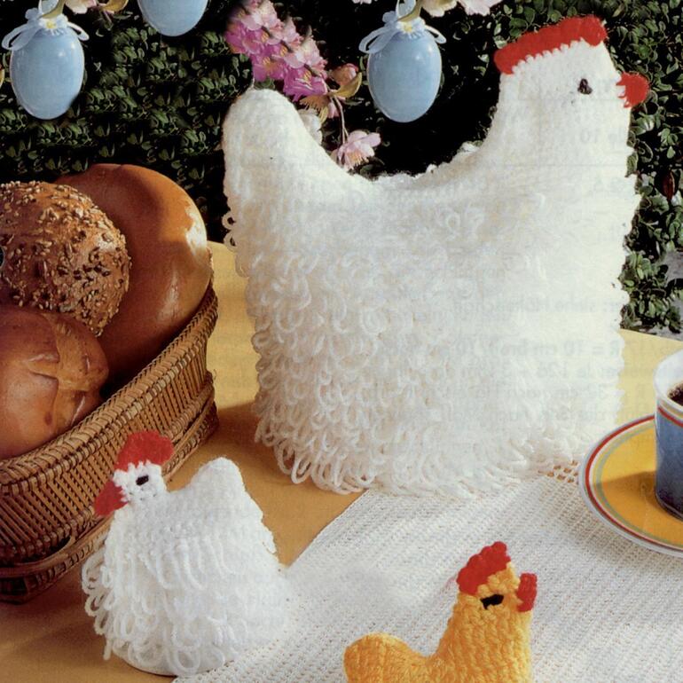 Gehäkelte weiße Henne als Brotkorb mit rotem Kamm und zwei Küken daneben.