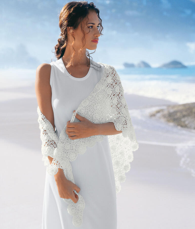 Frau trägt ein gehäkeltes Dreiecktuch aus weißem Garn, am Strand.