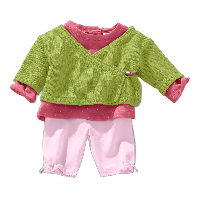 Wickeljacke in Grün und Pink mit einem Holzknopf, auf einem weißen Untergrund.