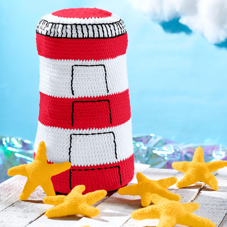 Gehäkelter Leuchtturm mit gelben Seesternen auf Holzuntergrund.