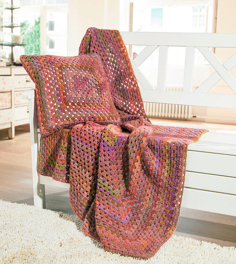 Bunte Decke und Kissen aus Scala auf einer Bank.