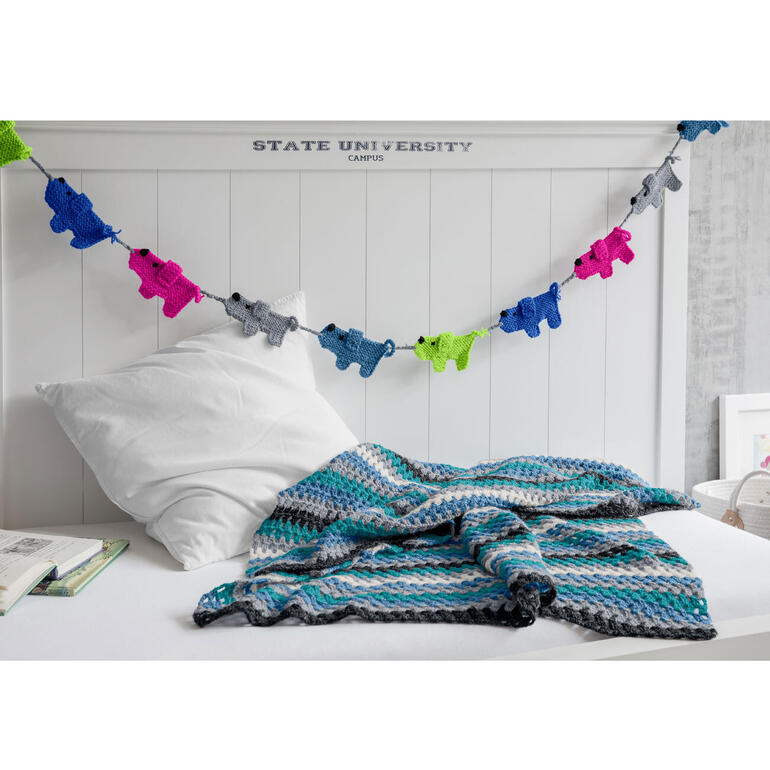 Gehäkelte Decke in Blau- und Grautönen auf einem Bett.